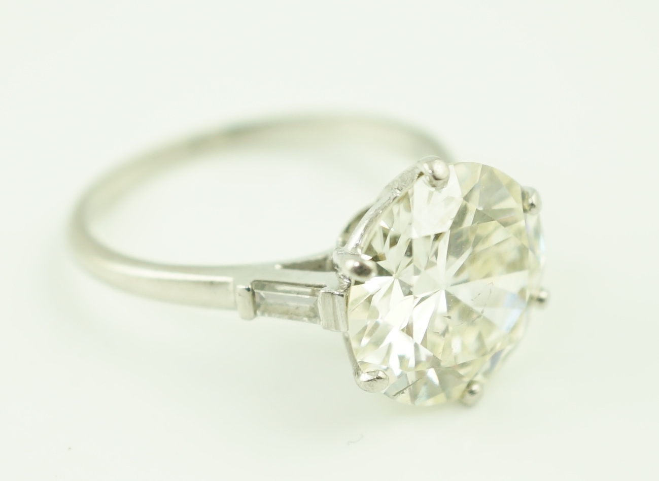 A platinum and single stone diamond set ring, with baguette cut diamond set shoulders